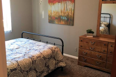 bedroom with bed that has a black and white circle bedspread, a brown dresser and painting on wall