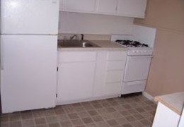 apartment kitchen with tan walls and white black splash, white appliances, and cupboards