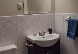 apartment bathroom with grey walls, white toilet, and vanity with a white sink and a mirror and lighting above it