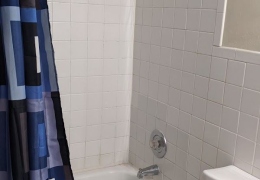 apartment bathroom with white square tiling, white toilet, and white tile shower and bath combo