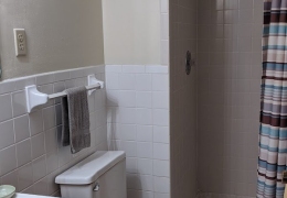 apartment bathroom with white square tiling, cream walls, white toilet, and white tile shower and bath combo