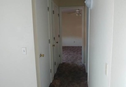 hallway leading to a bedroom it is lined with dark carpet and cream walls. there are white closet doors along one wall