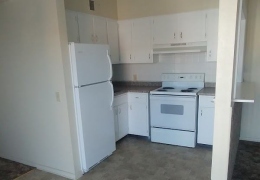 apartment kitchen and dining area with tan walls and white black splash, white appliances, and cupboards