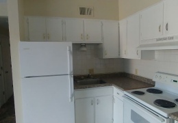 apartment kitchen with tan walls and white black splash, white appliances, and cupboards