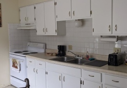 apartment kitchen with tan walls and white black splash, white appliances, and cupboards