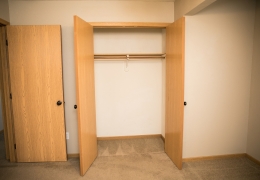 walk in closet of an apartment bedroom with light grey carpet and walls the doors are open and it is empty of clothing as the apartment is ready for rent