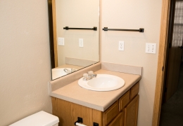 apartment bathroom with grey walls white toilet and vanity with a white sink and a mirror and lighting above it