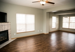 living room of an apartment with wood floors, grey walls and black fireplace with marble trim there is light flowing in from the windows and it is empty of furniture and ready for rent