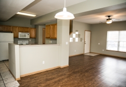 dining room and kitchen area of an apartment with wood and tile floors the walls are grey and the kitchen appliances are white there is light flowing in from the windows and it is empty of furniture and ready for rent