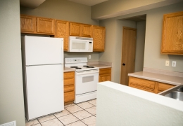 apartment kitchen with grey walls, white appliances, light brown cupboards, and white tile floor