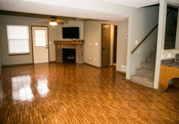 living room of an apartment with wood floors grey walls and fireplace with brick trim there is light flowing in from the windows and it is empty of furniture and ready for rent