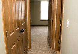 hallway leading to a bedroom it is lined with grey carpet and grey walls there are brown closet doors along one wall