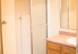 apartment bathroom with brown tile floor a vanity with white sink and a shower with a sliding door