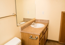 apartment bathroom with grey walls, white toilet, and vanity with a white sink and a mirror and lighting above it