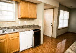 apartment kitchen with grey walls white appliances light brown cupboards and wood floor there is light flowing in from the windows and it is empty and ready for rent
