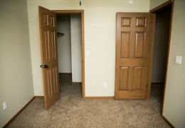 apartment bedroom with light grey carpet and walls and light brown closet doors it is empty of furniture and ready to rent