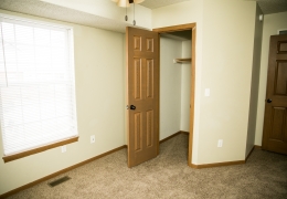 apartment bedroom with light grey carpet and walls a ceiling fan and light brown closet doors there is light flowing in from the windows and it is empty of furniture and ready for rent